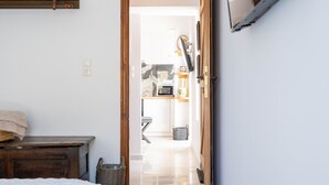 Una camera da letto con un letto, un comodino in legno, una TV a parete e un corridoio che conduce a una zona cucina.
