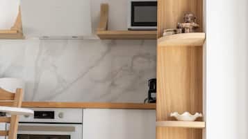 Une cuisine moderne avec des meubles blancs, un four encastré, un four à micro-ondes et une étagère en bois où sont disposés des objets décoratifs.
