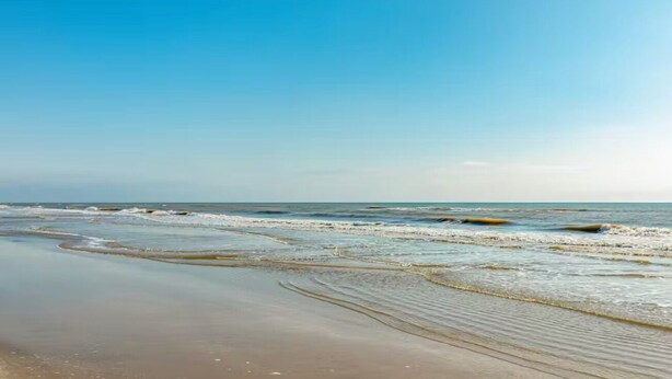 Een strand met rustige golven en een heldere lucht.