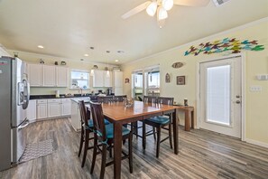 A spacious kitchen with white cabinets, a wooden dining table, and a ceiling fan. - Pelican View at Crystal Beach (Bolivar Peninsula)