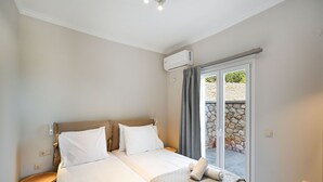 Habitación de hotel con dos camas, una mesita de noche de madera, una pequeña mesa y vistas a un muro de piedra y vegetación a través de una puerta corrediza.