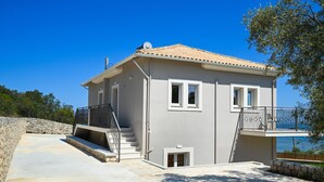 Une maison à deux étages avec un balcon, un mur en pierre et une vue sur la mer.