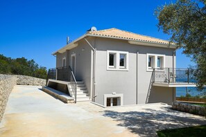 A two-story house with a balcony, a stone wall, and a view of the sea. - Lainas Sea View Lefkada 3 (Frini)
