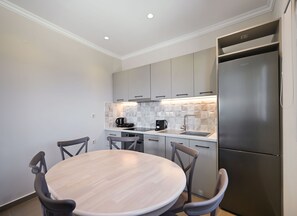 A modern kitchen with a round dining table and four chairs, a built-in oven, and a stainless steel refrigerator. - Lainas Sea View Lefkada 4 (Frini)