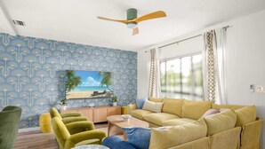 Un salon comprenant un canapé, des fauteuils, une table basse, un téléviseur et un ventilateur de plafond.