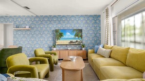 Un salon avec un papier peint à motifs bleus, un meuble en bois, un canapé jaune et un fauteuil vert.