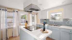 Une cuisine moderne dotée d’un îlot central, d’une cuisinière intégrée, d’une grande fenêtre et d’un évier.