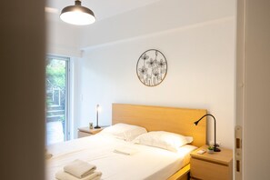 Ein ordentlich bezogenes Bett mit weißen Leinen, eine Nachttischlampe und ein an der Wand hängendes Kunstwerk.