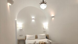 A bedroom with a large bed, two bedside tables, a nightstand, a wooden bench, and a chandelier. - Dreamer's secret villa II (Emporio)