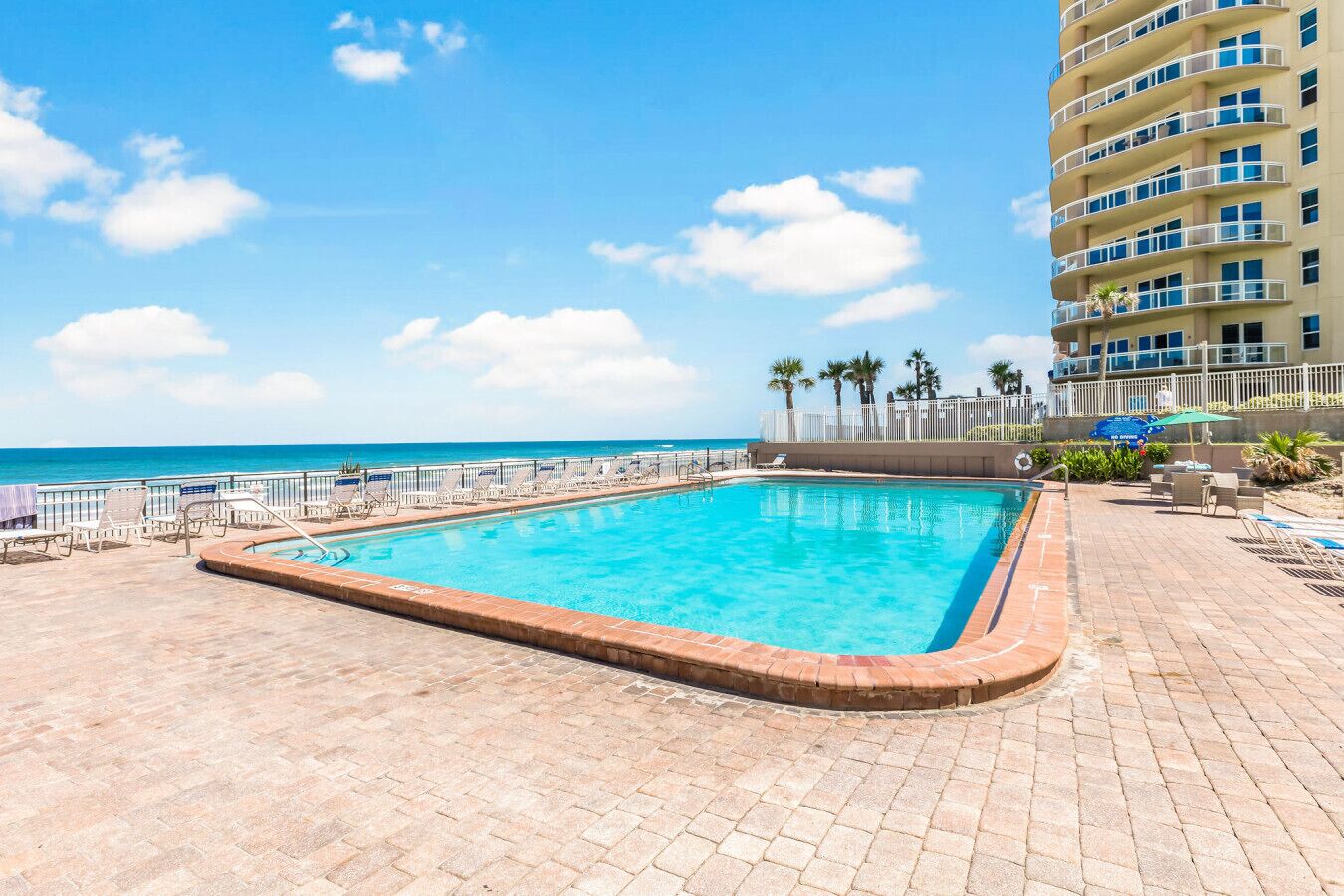 Una piscina rectangular con un borde de baldosas, rodeada de sillones de descanso y una valla.