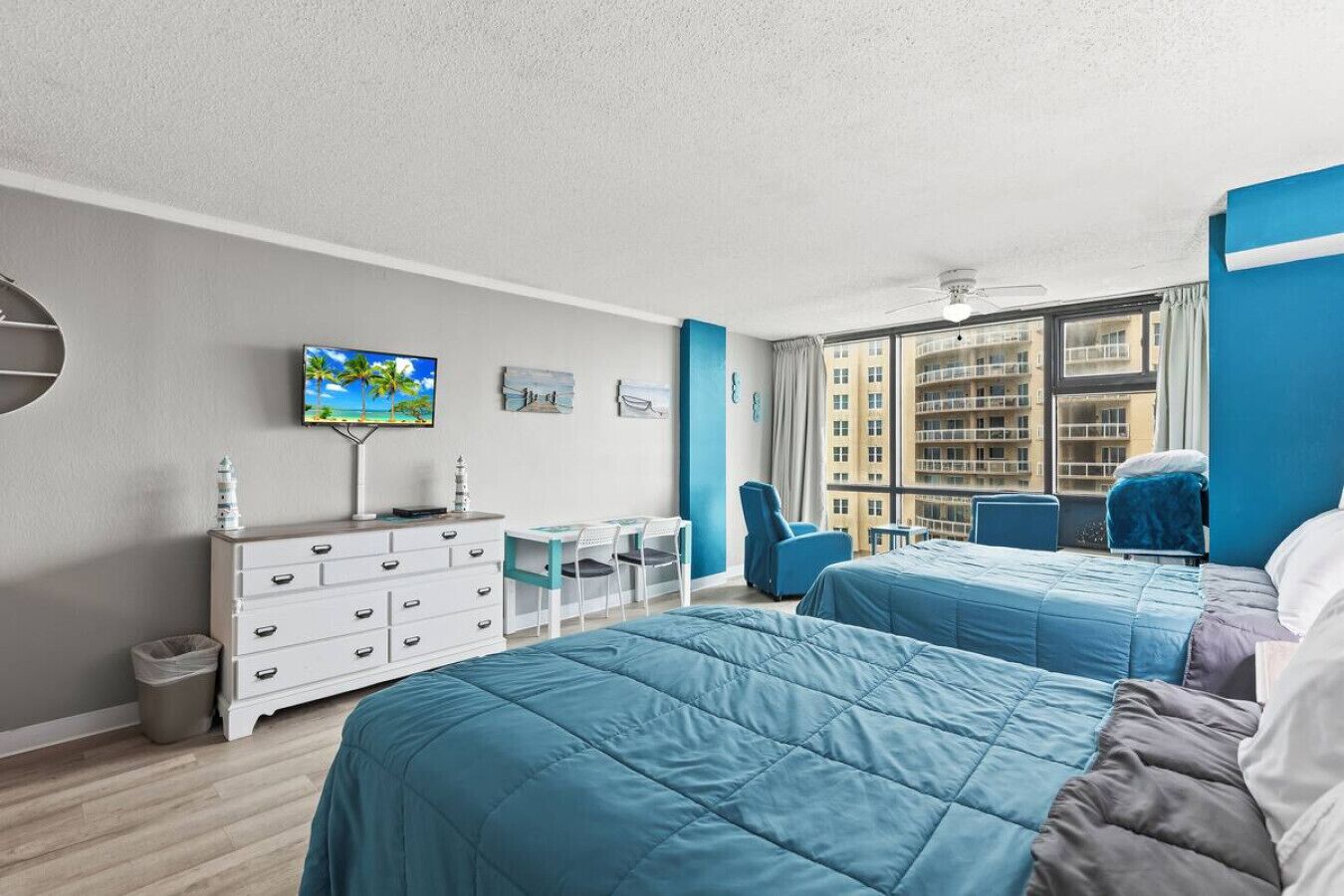 A hotel room with two beds, a desk, a chair, a TV, and a view of the city.