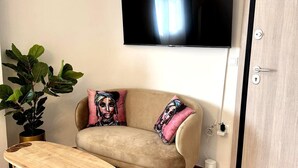 A living room with a sofa, a flat-screen TV, a coffee table, a potted plant, and a door. - Athenian Stay Chara's 2 Apartment (Neo Psichiko)