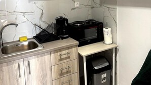 A compact kitchen with light wood cabinets, a stainless steel sink, a black coffee maker, a microwave, and a trash bin. - Athenian Stay Chara's 2 Apartment (Neo Psichiko)