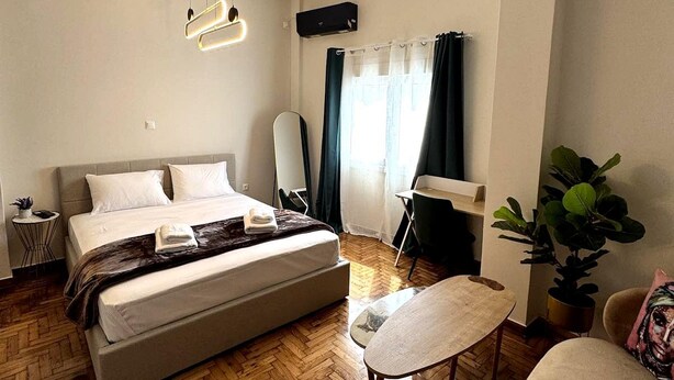 A modern hotel room with a large bed, a small table, a chair, and a potted plant. - Athenian Stay Chara's 2 Apartment (Neo Psichiko)