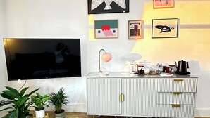 Ett vardagsrum med en platt-TV, ett vitt skåp med en rosa lampa och flera inramade konstverk på väggen.