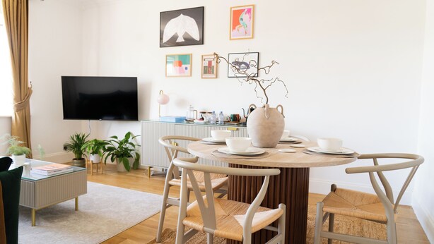 Ett modernt vardagsrum med ett runt matbord, vita stolar, en platt-TV och konstverk på väggen.