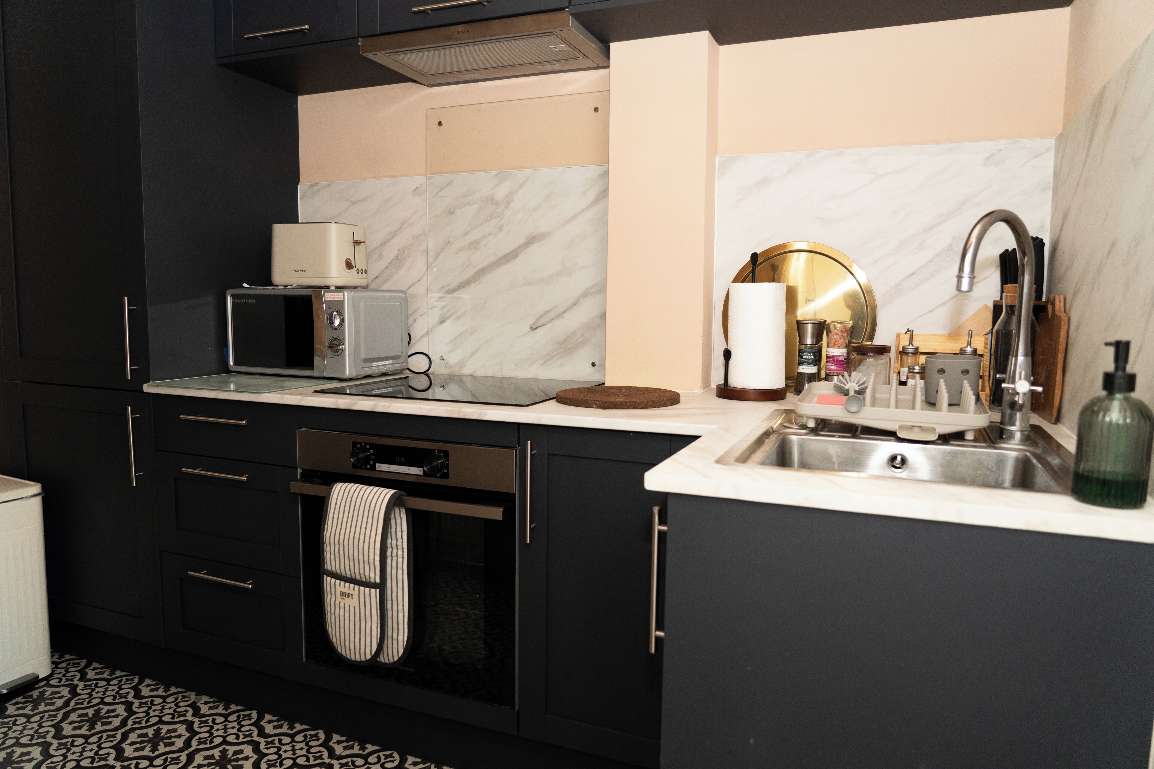 Una cucina moderna con mobili scuri, un forno a microonde, un tostapane, un lavello e un pavimento a motivi.