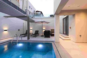 Un espace piscine intérieur moderne, doté d’une piscine à eau claire, de chaises longues et d’une petite table.