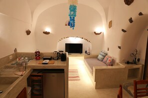 Un espace de vie compact comprenant un coin cuisine, un canapé, un téléviseur et un luminaire décoratif suspendu.