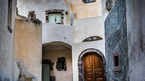 Ein schmaler Gang mit Steinwänden, einer Holztür und einer Treppe, die zu einem Balkon im zweiten Stock führt.