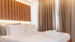 Una cama bien hecha con sábanas blancas, cabecero de madera y cortinas color beige.