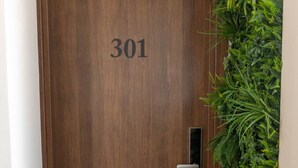 Una porta de fusta amb el número 301, un pom modern i una paret vertical plena de plantes verdes al costat.