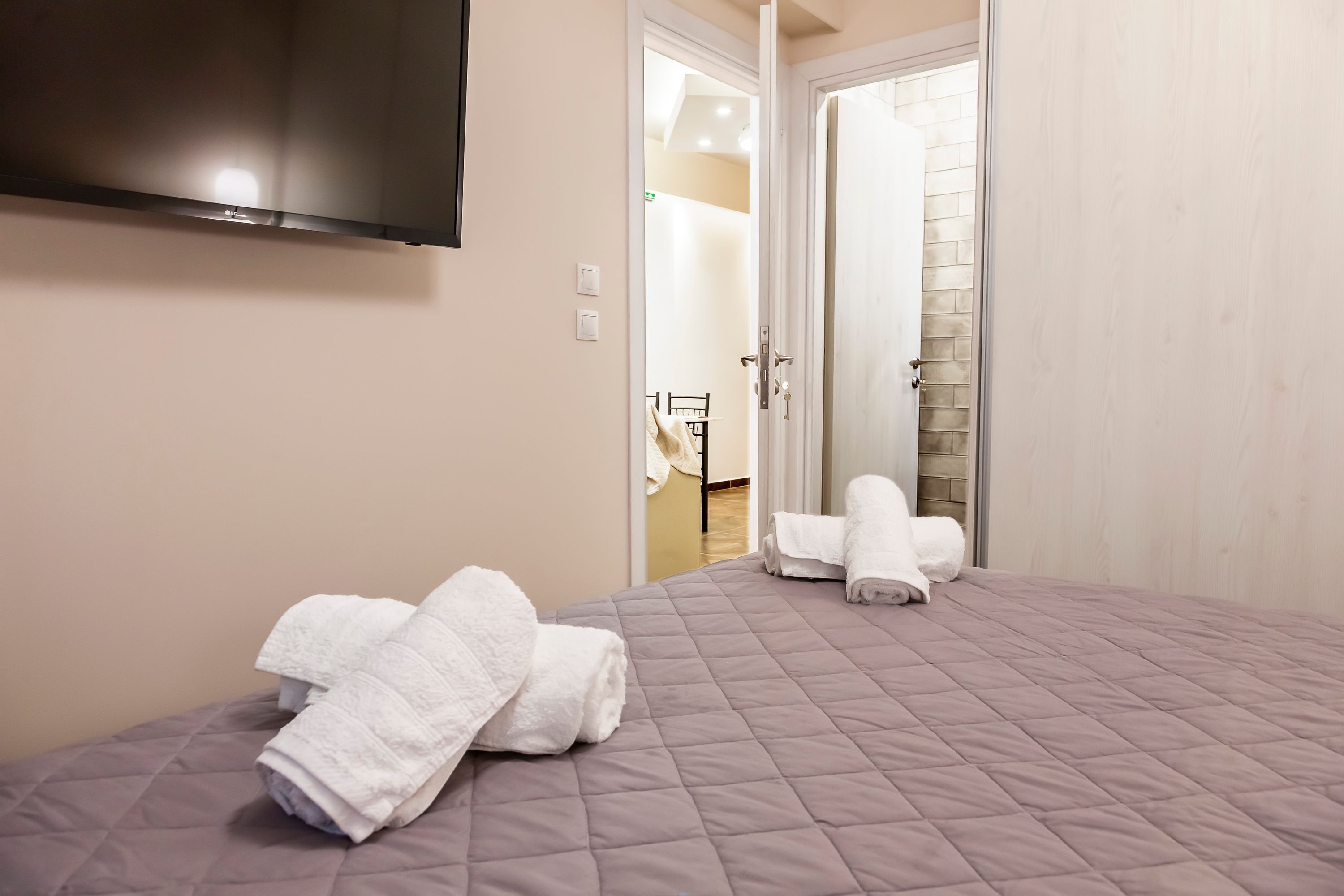 Ett hotellrum med en säng, en tv som är monterad på väggen och en dörr som leder till ett annat rum.