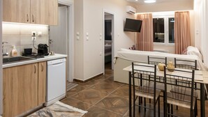 Habitación de hotel compacta con kitchenette, zona de comedor, cama y televisión montada en la pared.