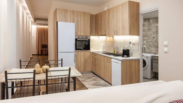 Una cocina moderna con armarios de madera, un comedor con mesa y sillas, un refrigerador, un horno, una lavadora y un lavavajillas.
