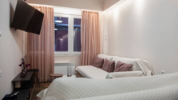 Quarto de hotel com duas camas, televisão de tela plana na parede, escrivaninha com cadeira, mesinha e janela com cortinas.