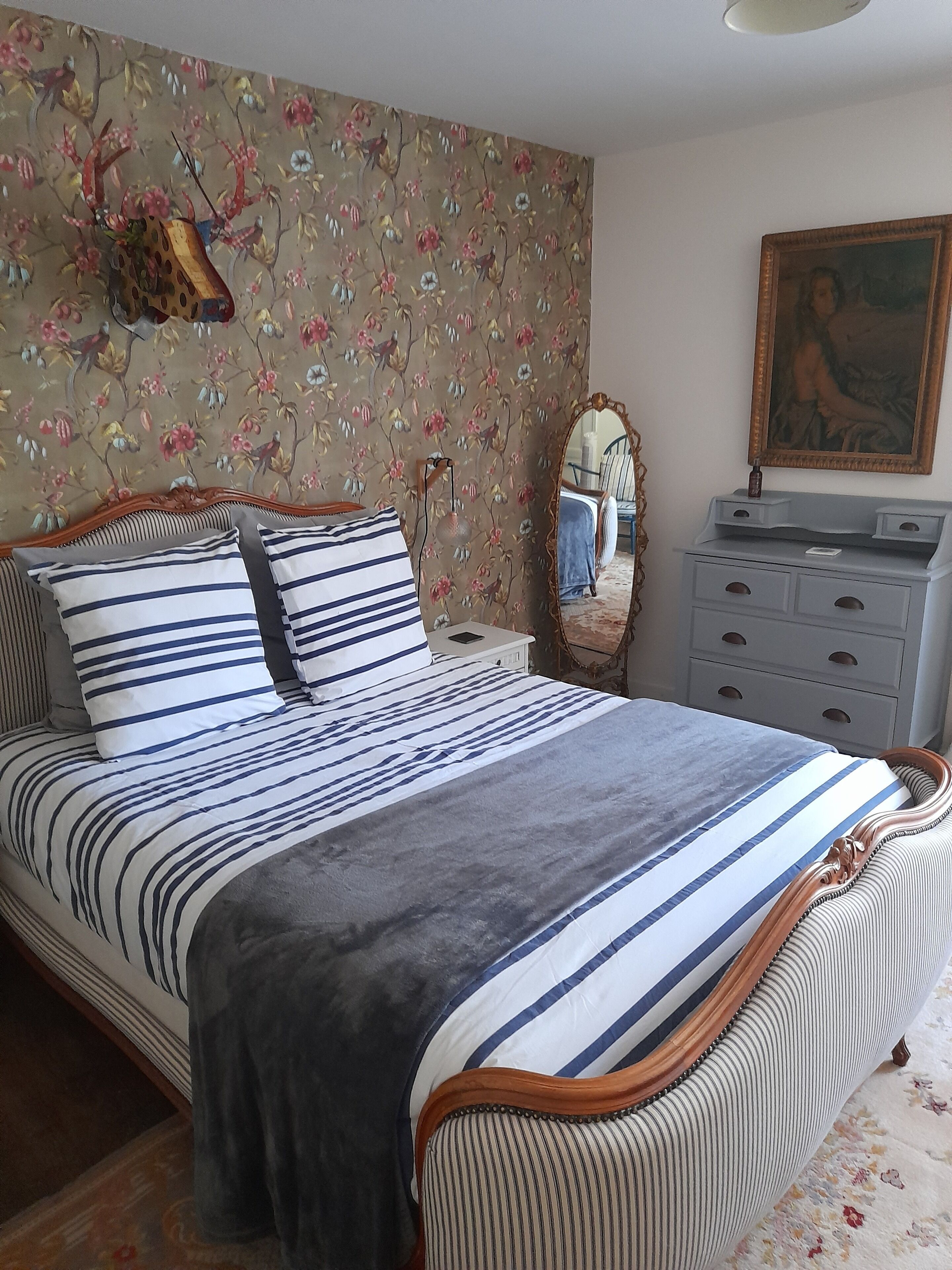 A bedroom with a bed, a dresser, a mirror, and a floral wallpaper.