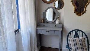 Ein Zimmer mit Schminktisch, zwei Spiegeln, einem Sessel und einem gemusterten Teppich.