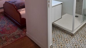 Ein Schlafzimmer mit einem Bett, einem Nachttisch, einem Spiegel und einem Fenster mit Vorhängen.