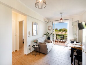 Un salon moderne avec un canapé, une petite table sur laquelle repose un plateau, une plante en pot et une vue sur l’extérieur.