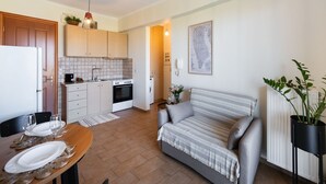 Un espacio habitable compacto con kitchenette, comedor, sofá y una planta en maceta.