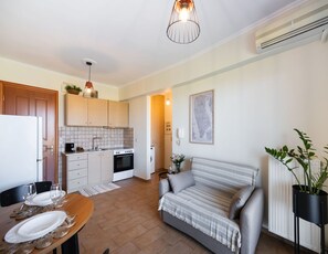 A compact living space with a kitchenette, a dining area, a sofa, and a potted plant. - Casa Vardani 1 Modern Central Apartment (Lefkada)