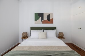 Una cama bien hecha con cabecera verde, dos lámparas de noche y un cuadro en la pared.