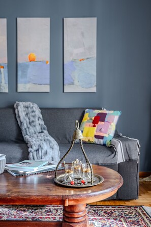 Ein Wohnzimmer mit grauem Sofa, einem farbenfrohen gesteppten Kissen, einem Holztisch mit dekorativem Metallstück und einem gemusterten Teppich.