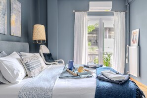 Ein ordentlich bezogenes Bett mit Kissen, ein Tablett mit Tassen und einem Buch, sowie ein Fenster mit Vorhängen.