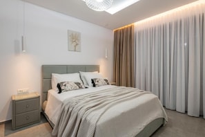 Ein modernes Schlafzimmer mit Bett, Nachttischen und einem großen Fenster mit Vorhängen.