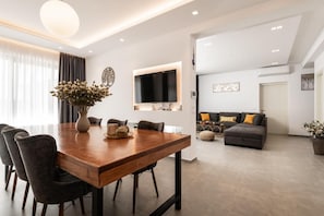 Ein modernes Wohnzimmer mit einem Holzesstisch, grauen Sofas und einem an der Wand befestigten Flachbildfernseher.