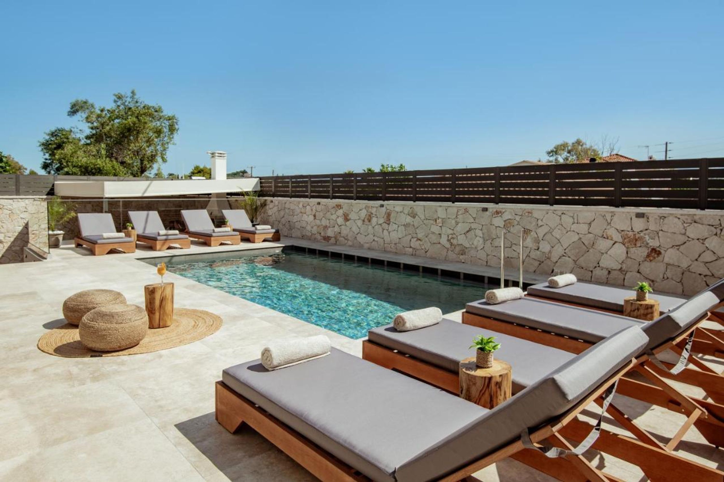 Un área junto a la piscina con sillones de descanso, un muro de piedra y una piscina cristalina.