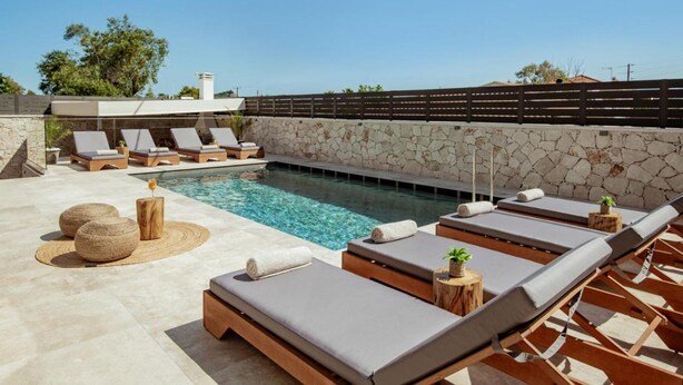 Un área junto a la piscina con sillones de descanso, un muro de piedra y una piscina cristalina.