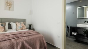 Un dormitorio con cama, mesita de noche y un velador con una planta.