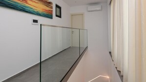 Un pasillo moderno con barandilla de vidrio, un cuadro abstracto grande y una puerta al final.