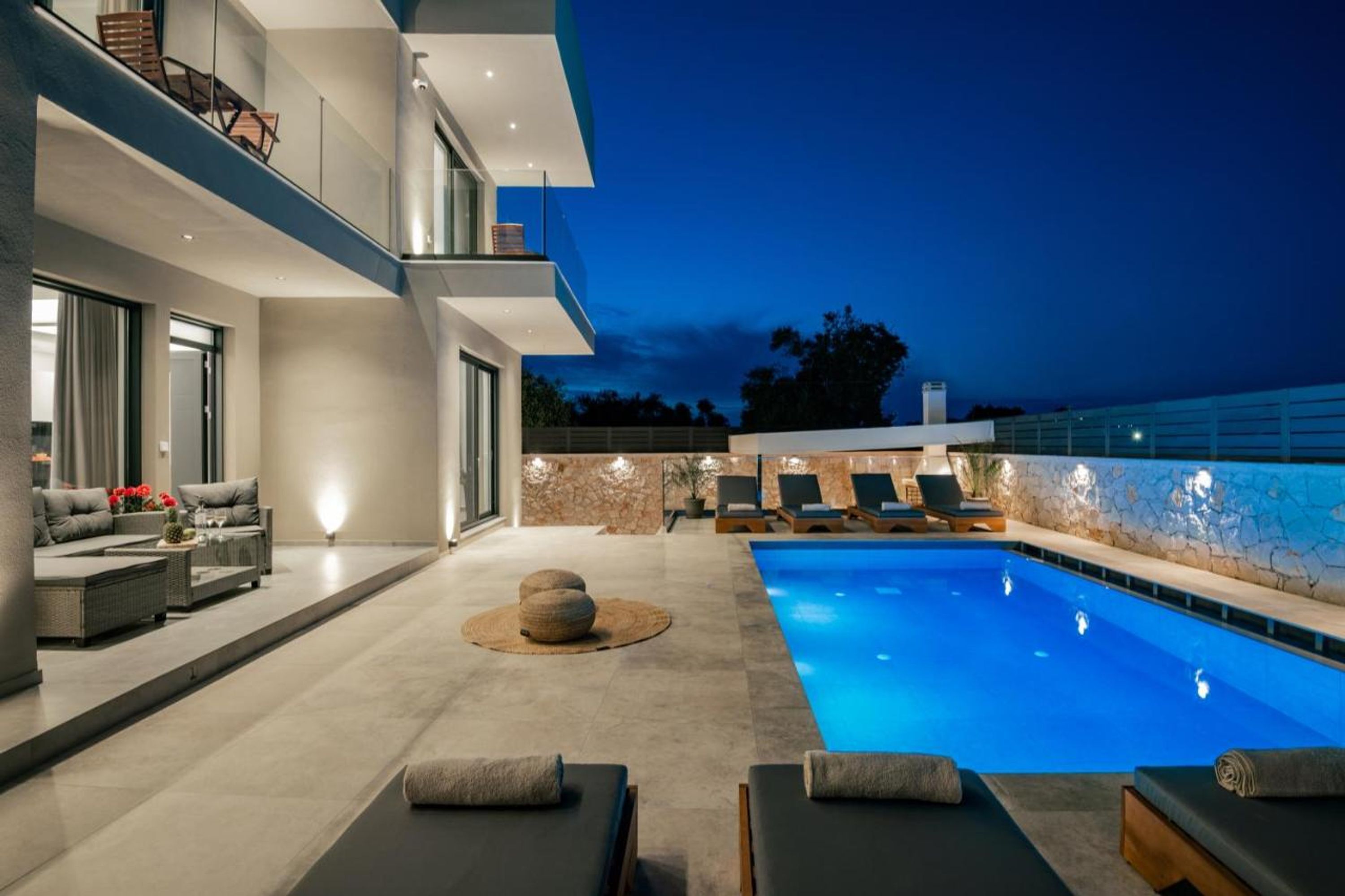 A modern outdoor pool area with lounge chairs, a sofa, and a stone wall.