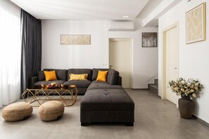 A modern living room with a grey sectional sofa, two poufs, a coffee table, and a vase of flowers. - Villa Artemis in Zakynthos (Agios Sostis)
