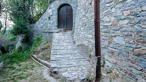 Eine steile Steintreppe führt zu einer Holztür, umgeben von Steinmauern und Grünpflanzen.