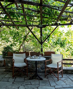 A stone-floored outdoor seating area with two wooden chairs and a small round table, surrounded by a wooden pergola with climbing plants. - Secluded cottage & guesthouse in the mountains (Makrinitsa)