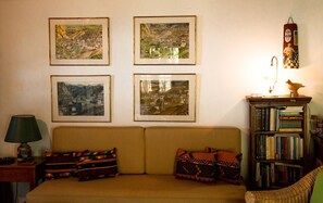 A living room with a sofa, four framed pictures on the wall, a lamp, a bookshelf, and a wall-mounted clock. - Secluded cottage & guesthouse in the mountains (Makrinitsa)